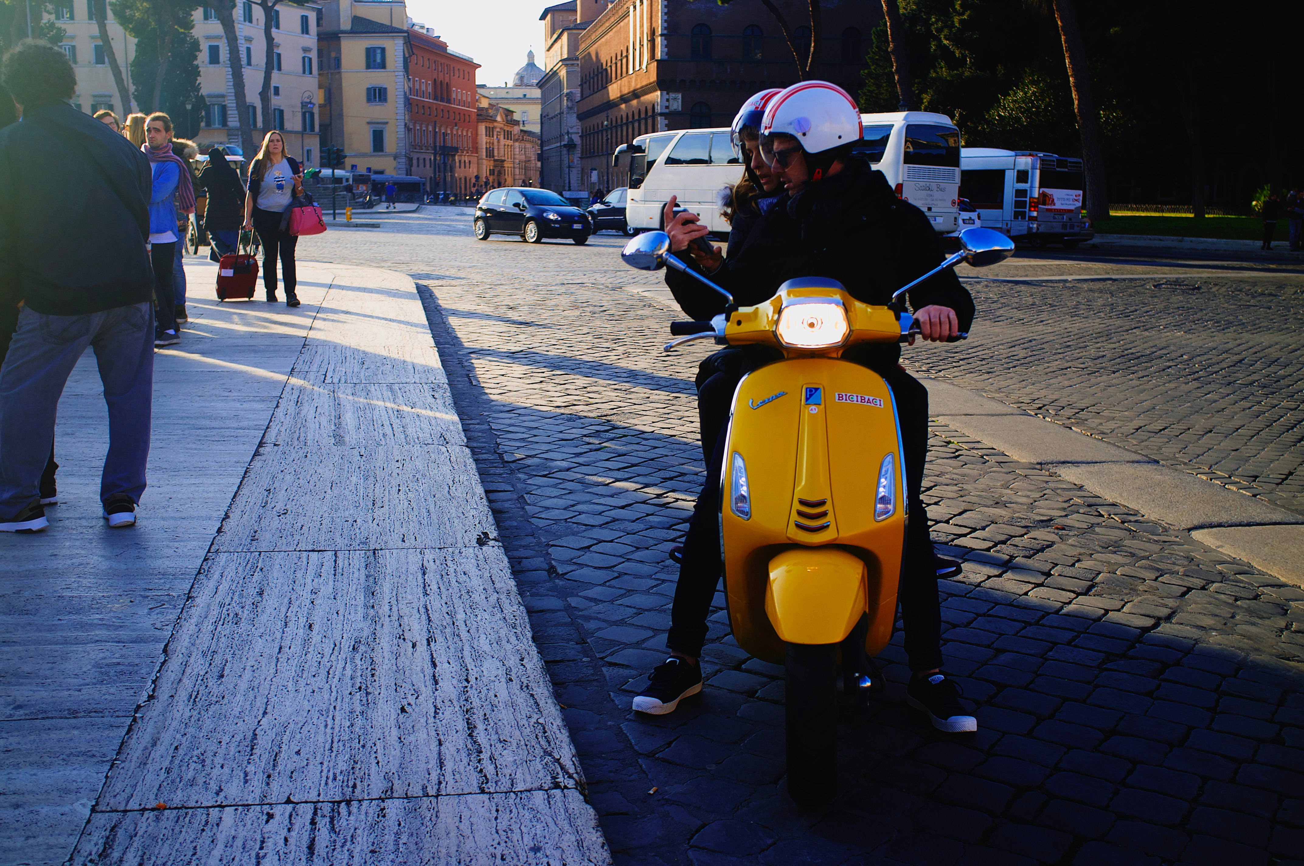 man in black jacket riding yellow motor scooter on gray wooden pathway during daytime